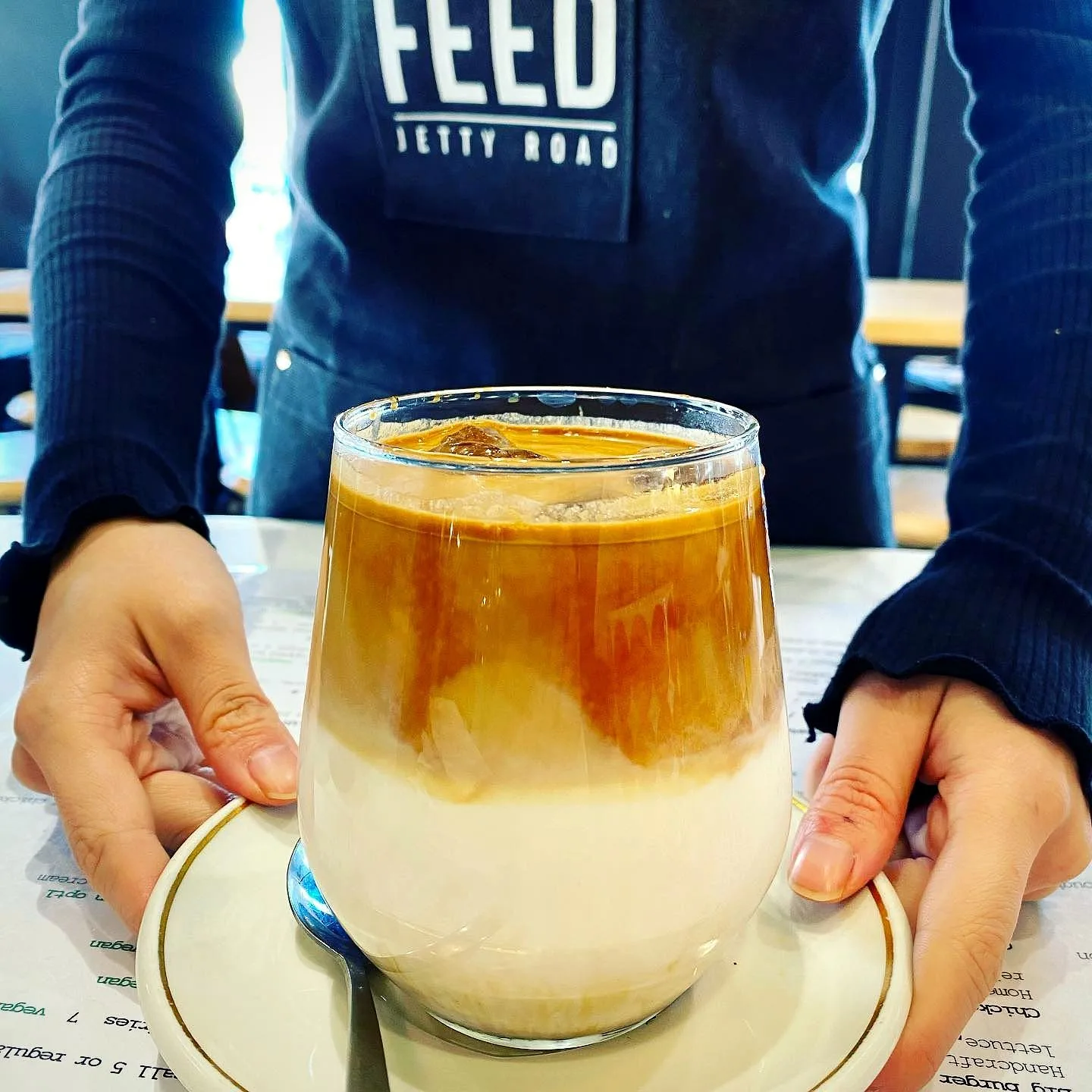 Iced latte held up in a Feed Jetty Road apron